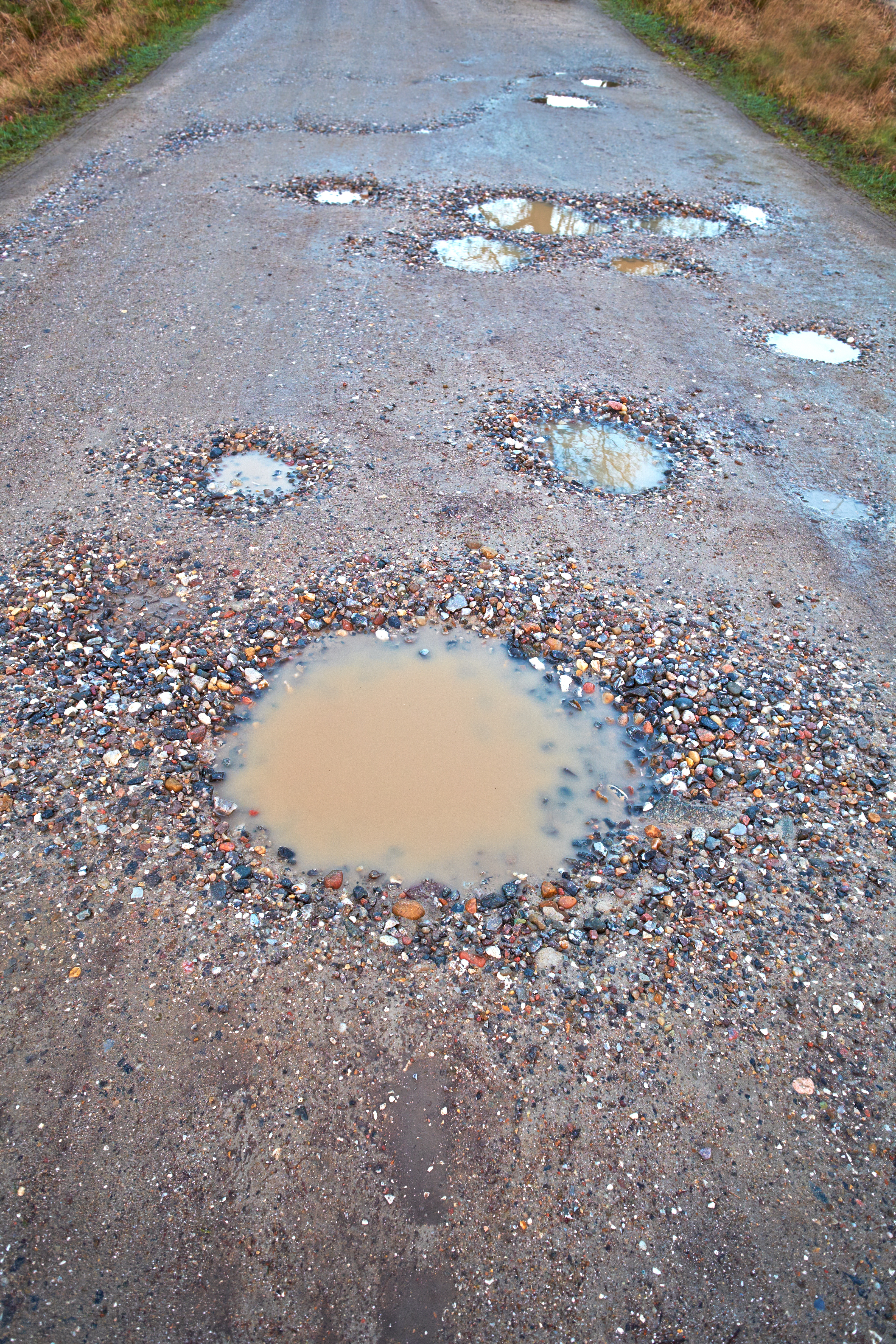 a gravel road with puddles and potholes